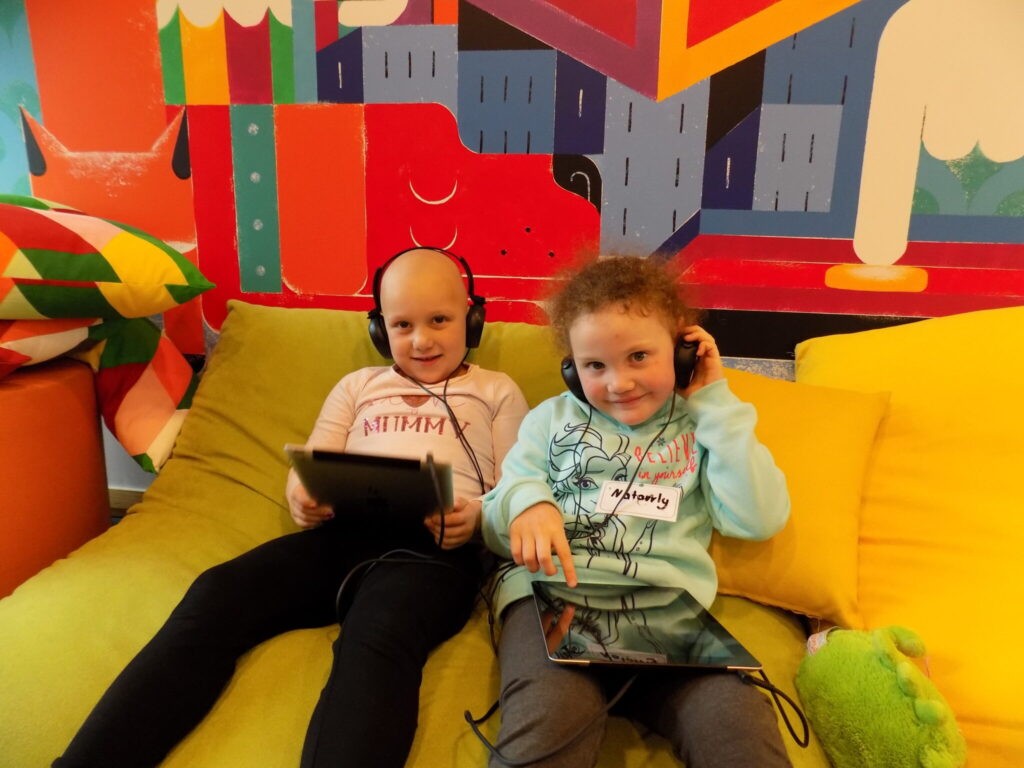 Photo of children wearing headphones and seated on a couch playing with tablet devices