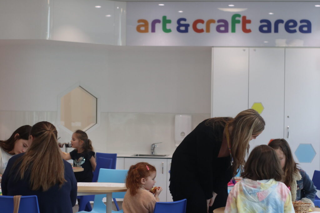 A photo of the arts and crafts area showing tables and chairs grouped around an art room with craft projects on them