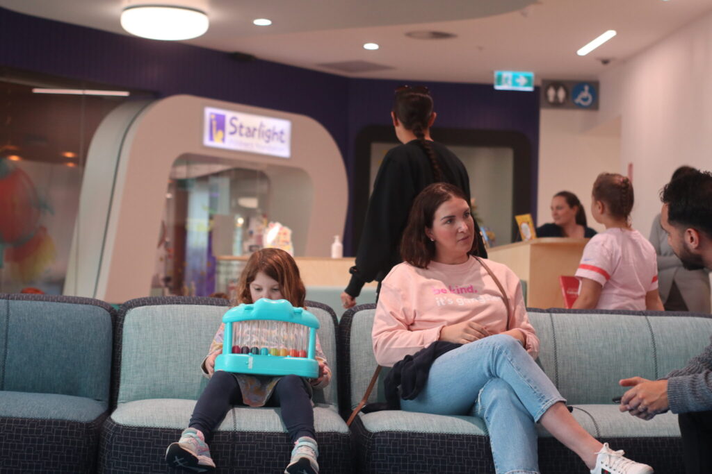 Photo of a parent and child sitting on a lounge together reading and playing tous