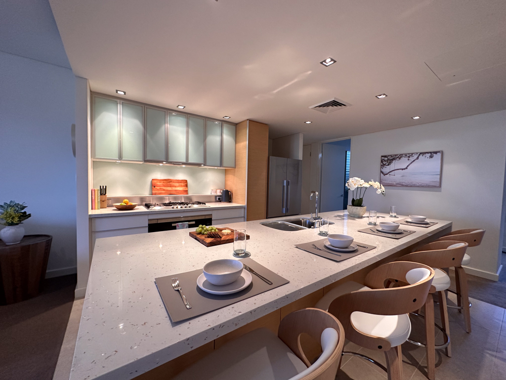 A photo of the kitchen in the Ronald McDonald Family Retreat in Mandurah, showing an island bench with seating and a sink, as well as the stove and fridge on counters opposite