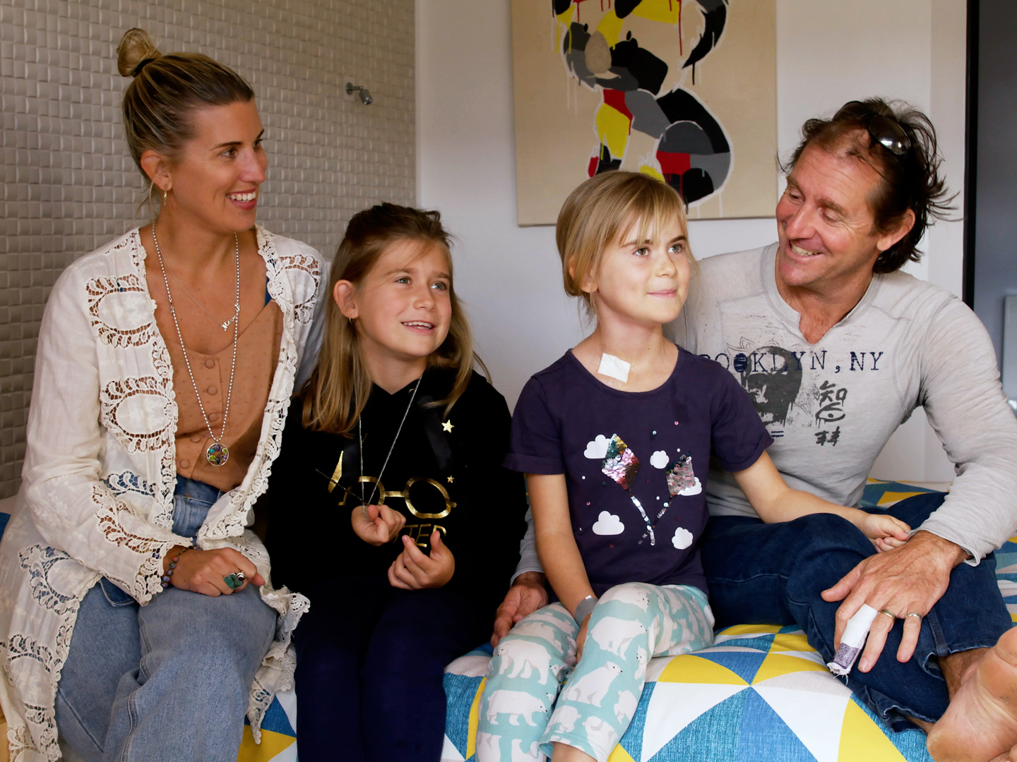 Photo of a family of four sitting on a bed in one of the rooms at Ronald McDonald House Nedlands.
